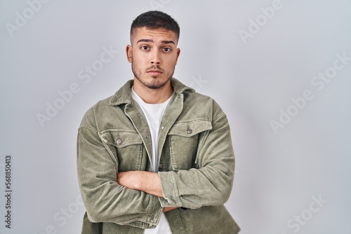 Young hispanic man standing over isolated background skeptic and nervous, disapproving expression on face with crossed arms. negative person.