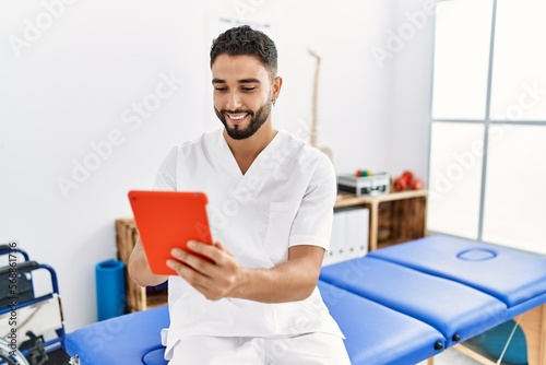 Young arab man wearing physiotherapist uniform using touchpad at clinic