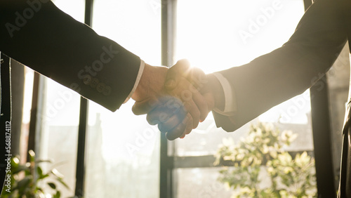 Close-up two men shake hands in office near window sunny sun background. Unrecognizable partners diverse businessmen conclude successful agreement support partnership cooperation greeting handshaking