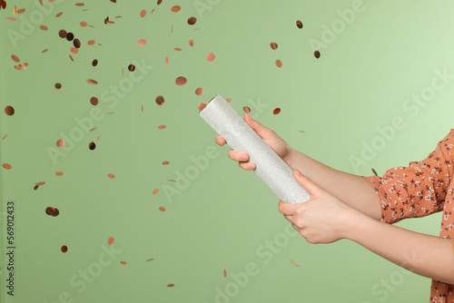 Young woman blowing up party popper on green background, closeup