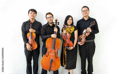 multiethnic group of musicians, string quartet posing for camera not playing. three men and a girl mixed group of musicians with wooden string instruments, standing against a white wall