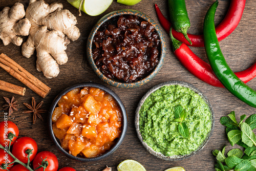 Indian chutney set in bowls on wooden background, top view