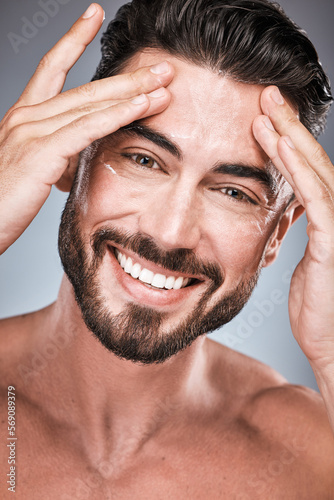 Face, skincare and man with cream in studio isolated on a gray background for facial wellness. Portrait, forehead cosmetics and happy male model apply lotion, healthy creme or moisturizer product.