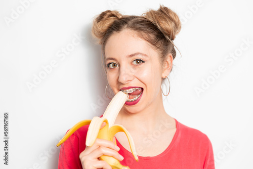 Young caucasian woman with two hair bundles wearing braces eating banana and enjoying it 