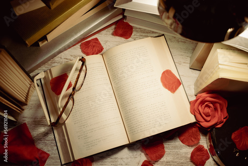 table with books, open book with glasses on top and rose petals