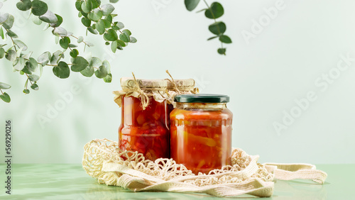 Probiotic foods. Eco friendly still life with pickled or fermented vegetables. Lecho and ajvar in glass jars on textile bag on blue background with leaves and shadows. Home food preserving or canning