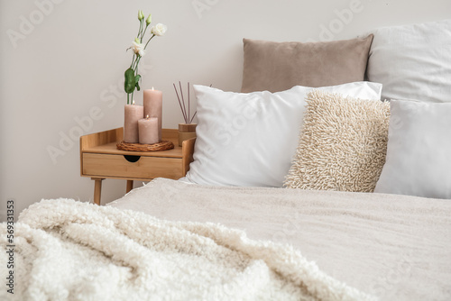 Burning candles, eustoma flower and reed diffuser on end table in bedroom