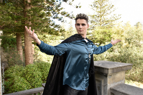 Close up portrait of handsome brunette man wearing fantasy medieval prince costume with golden crown and romantic silk shirt. historical castle location background.