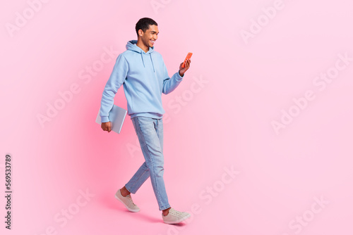Full length photo of attractive glad man user blogger wear trendy clothes go work typing sms empty space isolated on pink color background