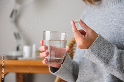 Closeup image of a woman holding white pills and a glass of water