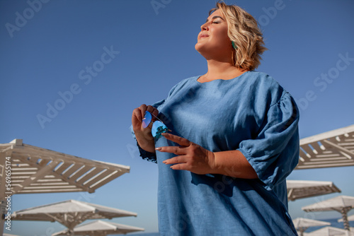 Beautiful woman plus size is walking against the background of nature in the sea. The adult woman is wearing a black maxi stylish dress. A woman of large size holds the cup pf coffee