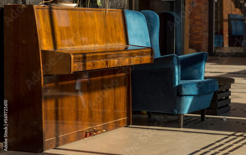 Stare pianino i niebieski fotel ( oraz stołek ze skrzynki po owocach) stoją na podłodze z ceramicznych płytek .