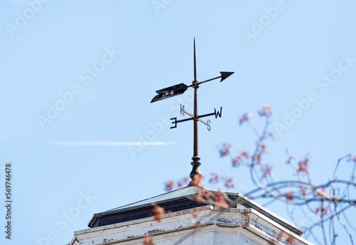 Old metal weather vane on the rooftop with cloudless sky pointing west