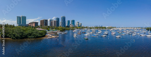 Coconut Grove Sailing Club at Dinner Key Marina at Miami, Florida in aerial panoramic view. There are boats on the blue waterfront of modern high-rise buildings against blue skyline.
