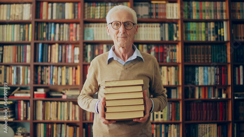 Portrait of smiling senior librarian holding a stack of books, knowledge, wisdom