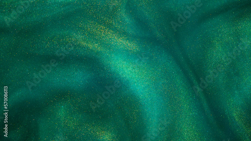 Abstract magic green background with golden sparkles. Photo of a green liquid with gold glitters. Various shades of green with golden splashes. Green backdrop with tints of golden glitters.