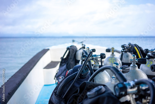 Scuba tanks are in the sharp foreground ready on a dive boat. In the background you can see the out of focus horizon, the sea and the cloudy sky as copy space