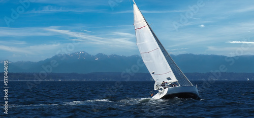 Isolated sailboat sailing into strong winds heeling over with speed in Elliott Bay near Seattle with Olympic Mountains in the background.