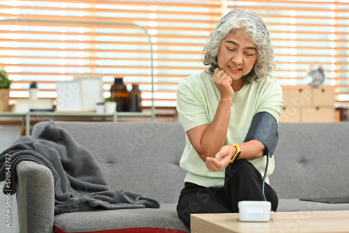 Smiling grey haired woman checking blood pressure with with digital pressure gauge at home