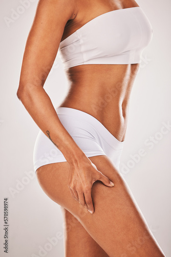Body, leg and cellulite with a model black woman in studio on a gray background posing in underwear. Wellness, natural and stretch marks with a female holding her thigh skin for beauty or skincare