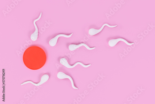 Abstract sperm cells swimming towards egg cell on pink background