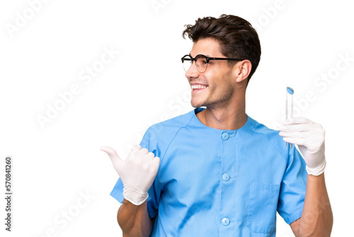 Young dentist man holding tools over isolated background pointing to the side to present a product