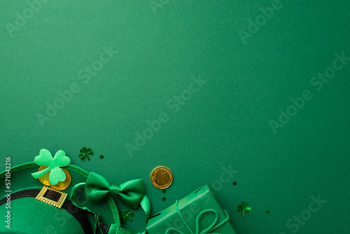 Saint Patrick's Day concept. Top view photo of leprechaun hat giftbox with bow gold coins bow-tie clover and trefoil shaped confetti on isolated green background with empty space
