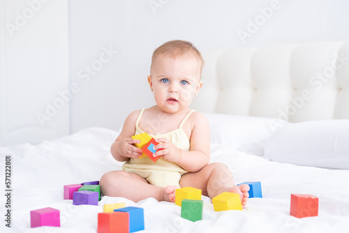 funny baby girl in yellow bodysuit playing with children wooden cubes on bed