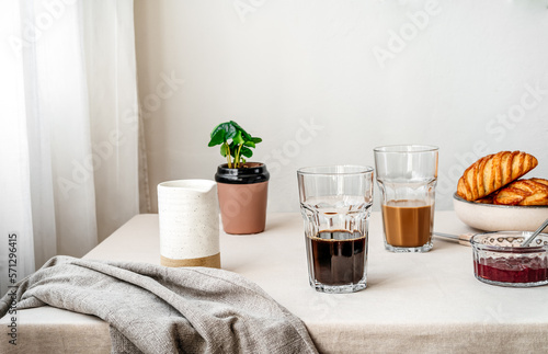 Spring cozy breakfast concept. Two glasses with coffee and milk, croissants, spring plant, jam, linen napkin. Kinfolk style