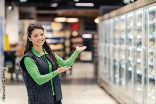 A friendly supermarket worker is showing retail place and welcoming customers.