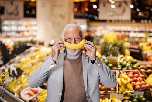 A silly old man is pretending banana is his mouth while looking at the camera.
