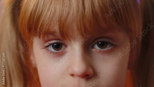 Extreme close-up macro portrait of smiling girl face. Teen beautiful kid's eyes looking at camera. Young positive toddler child opening wide her closed eyes. Brown eyes of blonde female children model