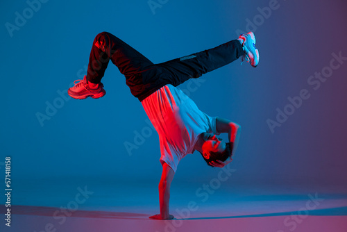 young guy dancer break dancing in neon red blue lighting, active energetic man doing acrobatic tricks, crazy moves