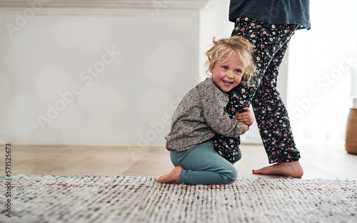 Happy, child clinging to leg of woman and playful fun and smile on carpet in home with mother. Little girl playing, laughing and joking with happiness, mom in pajamas and trust on floor in apartment.