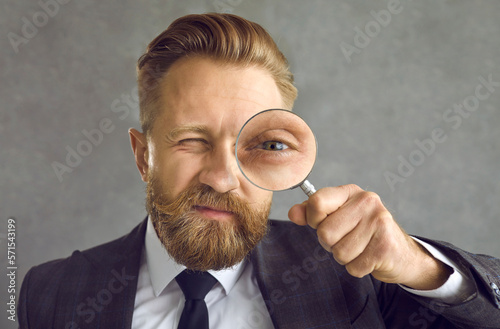Head shot handsome bearded young man in suit with magnifying glass in hand. Business expert looking for solution, hiring manager searching candidate, CEO controlling staff, entrepreneur making inquiry