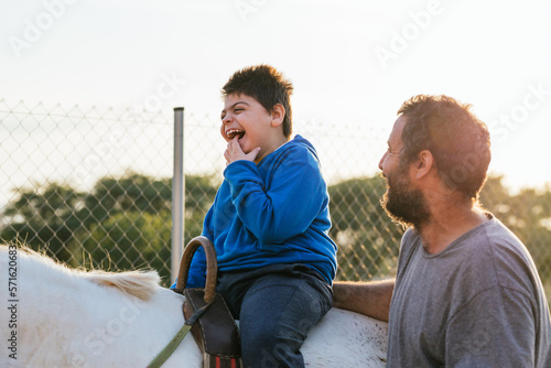 Child with disabilities enjoying having an equine assisted therapy in an equestrian center.