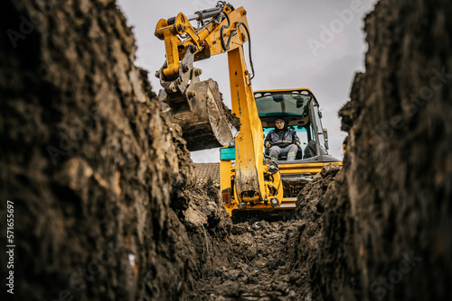 A worker in bulldozer is moving soil and making hole on construction site.