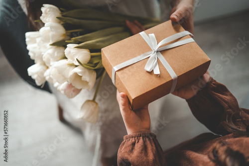 The child's hands hold a beautiful gift box with a ribbon and white tulips. Top view, close-up. Happy mother's day