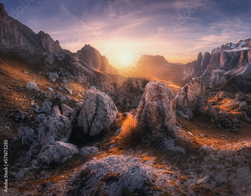 Rocks and stones at colorful sunset in autumn in Dolomites, Italy. Colorful landscape with mountains, trail on the hill, orange grass and trees, pink sky with clouds in fall. Hiking in mountains