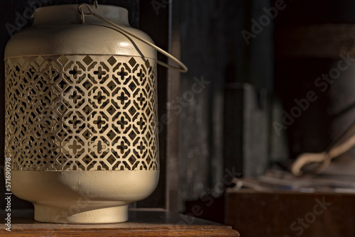 Stary lampion ze stalowej blachy , o ażurowej konstrukcji, stojący na nieco zakurzonej , drewnianej , lakierowanej półce . 