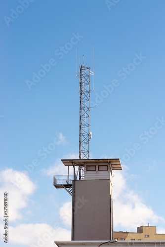 Wieża obserwacyjna z dużym masztem radiowym ( anteną) na płaskim dachu . Na tle błękitu nieba i chmur białych .