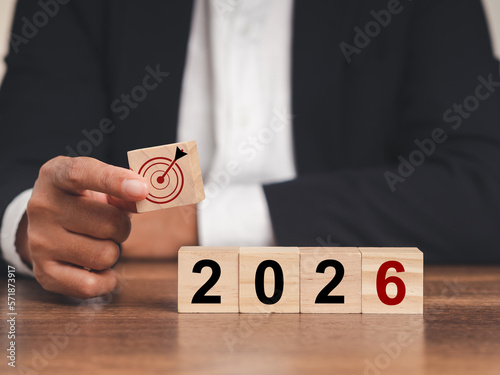 Business planning and strategy in 2026. Hand businessman holding wooden cubes with dartboard icon and wooden cubes with the letters 2026 on a table