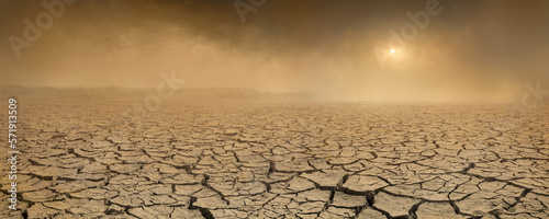 Wide panorama of barren cracked land with sun barely visible through the dust storm. Drought and desertification concept