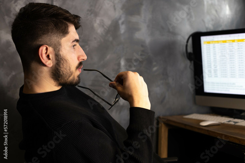 portrait d'un jeune employé de bureau ou homme d'affaires qui travaille devant son ordinateur. il réfléchit en mordillant ses lunettes