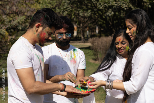 Friends family boys girls man woman celebrating enjoying holi festival of colors colours with gulal abeer color powder outdoor in a park, a popular hindu festival celebrated across india