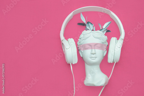 Plaster head with headphones on a pink background. A postcard with a place for text. Music.