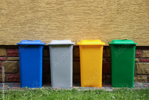 Many colorful recycling bins near yellow wall outdoors