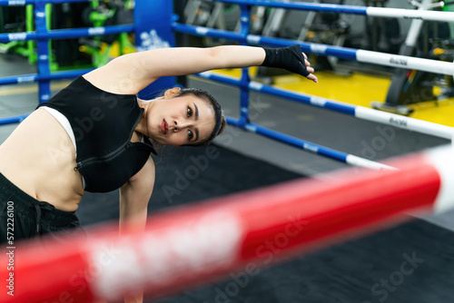 boxing woman stretching body wearing gloves on fighting ring. relax slim female athlete bend arms and hands warm body. calm muscular gym coach stretching body before exercise boxing training activity