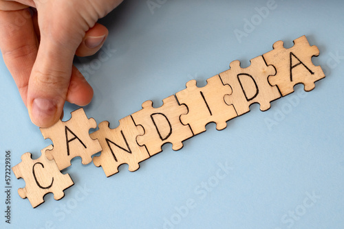 Candida is a word of wooden puzzles with letters, the concept of the parasitic fungus candida, blue background. Woman putting a puzzle together