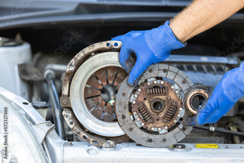 Automotive worker holding used car clutch disc, pressure plate and release bearing in front of the vehicle engine